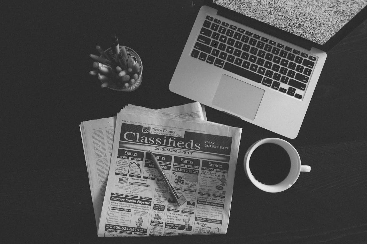 services-01 A black and white image of a laptop, newspaper, and coffee cup on a desk.